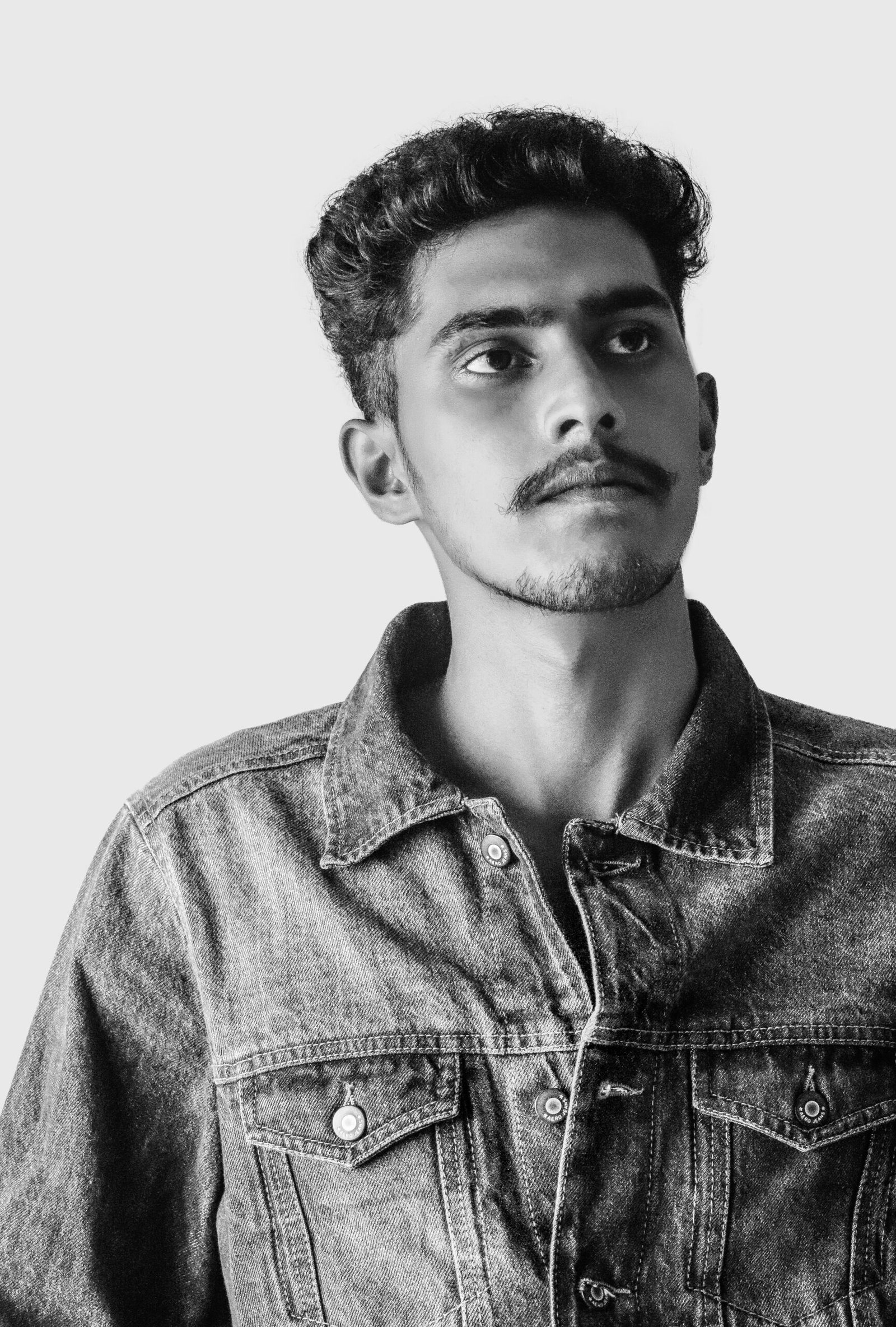 Artistic black and white portrait of a young man wearing a denim jacket, looking upwards.
